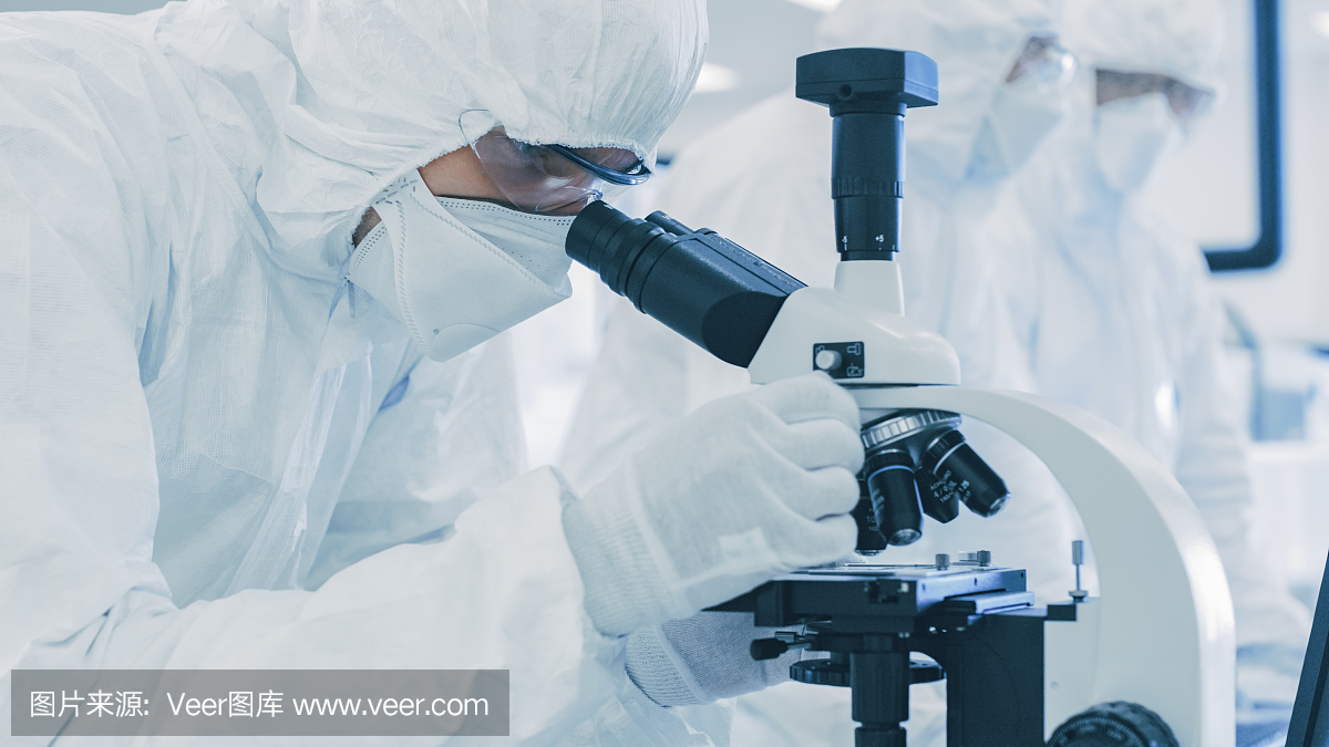 一个科学家在防护服做研究的特写镜头,使用显微镜在实验室。现代制造半导体和制药项目。